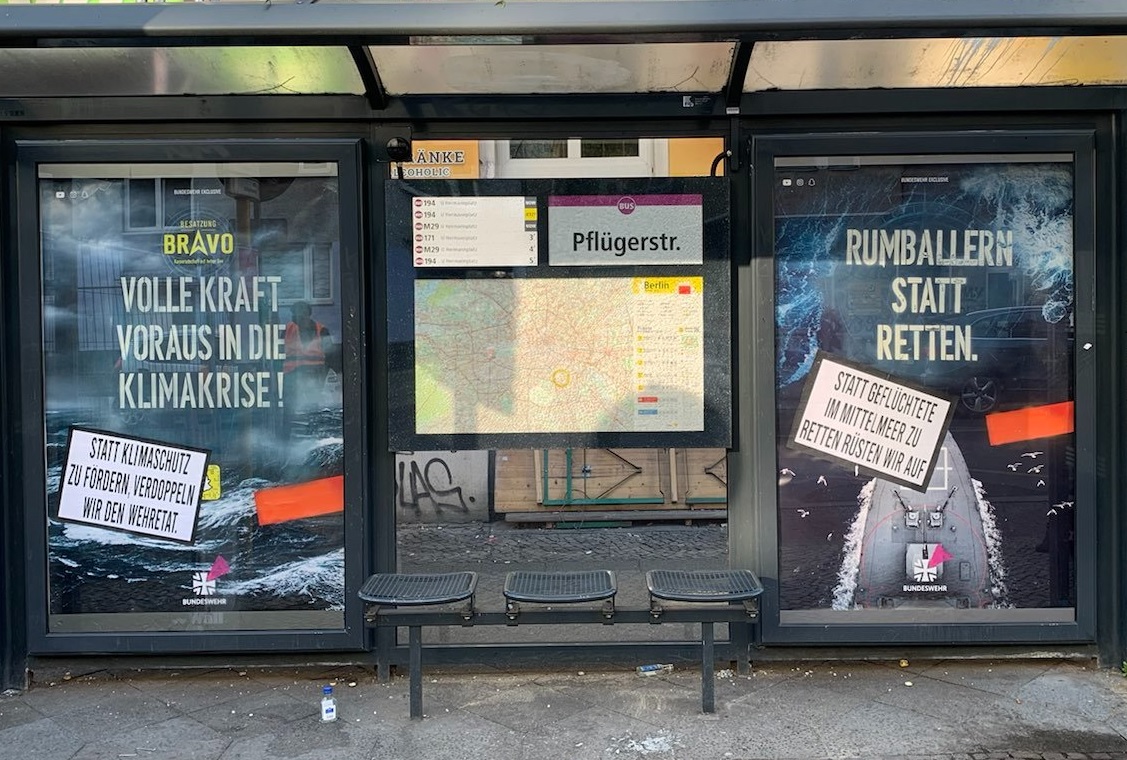 Auf dem Foto sind zwei Werbevitrinen in einer Berliner Bushaltestelle zu sehen, in denen Bundeswehr-Adbustings hängen. Angeprangert werden der fehlende Klimaschutz und die Unterlassung von Rettungseinsätzen für geflüchtete Menschen im Mittelmeer.